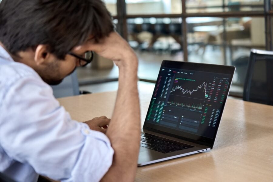 Stressed man examines a laptop with a stock market graph.
