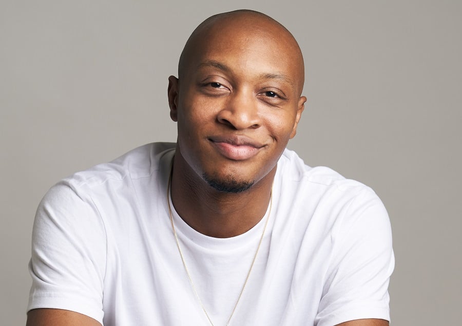 Bald man smiling in a white t-shirt and gold necklace.