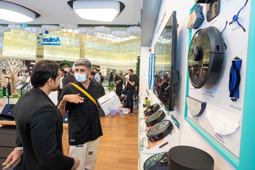 Two men talking near robotic vacuum cleaners in a bright mall.