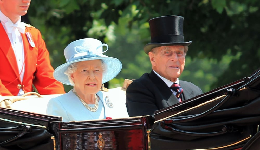 Royal couple in a horse-drawn carriage at an event.