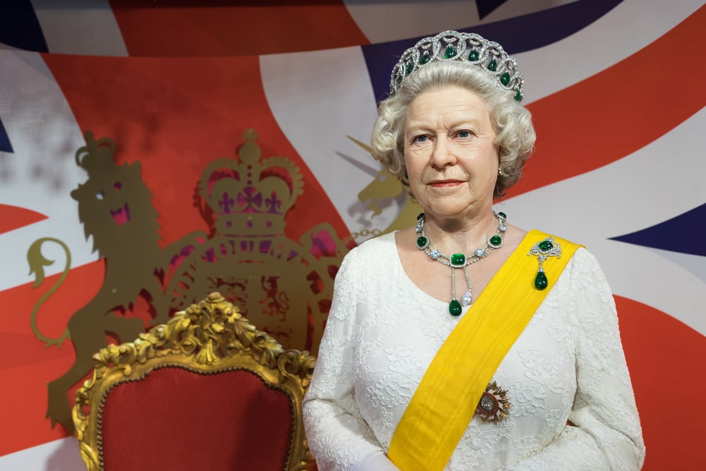 Wax figure of Queen Elizabeth II in royal attire before a throne.