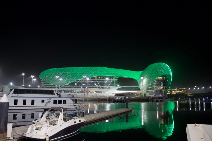 Motorboat docked at night near a green-lit building reflected in the water.