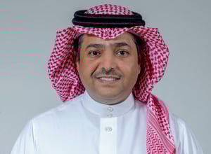 Man wearing Saudi attire smiling against a light gray background.