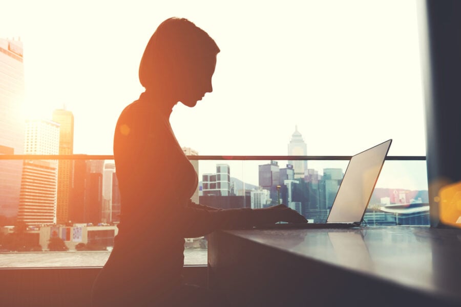 Woman using a laptop with a cityscape in the background.