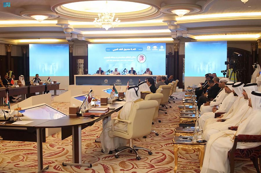 People in traditional attire at conference with large screen.