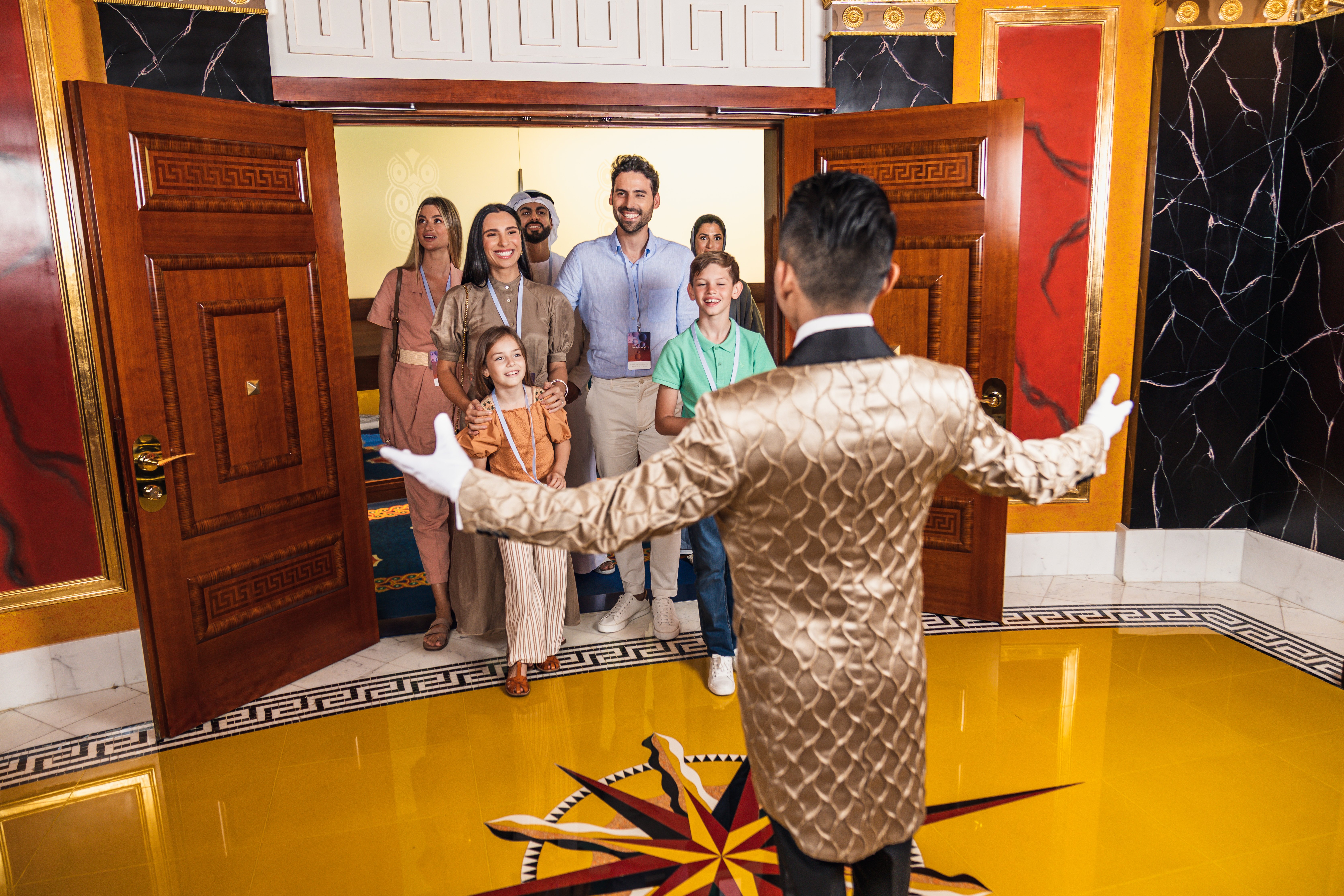 Man in gold jacket welcoming family in a luxurious hallway.