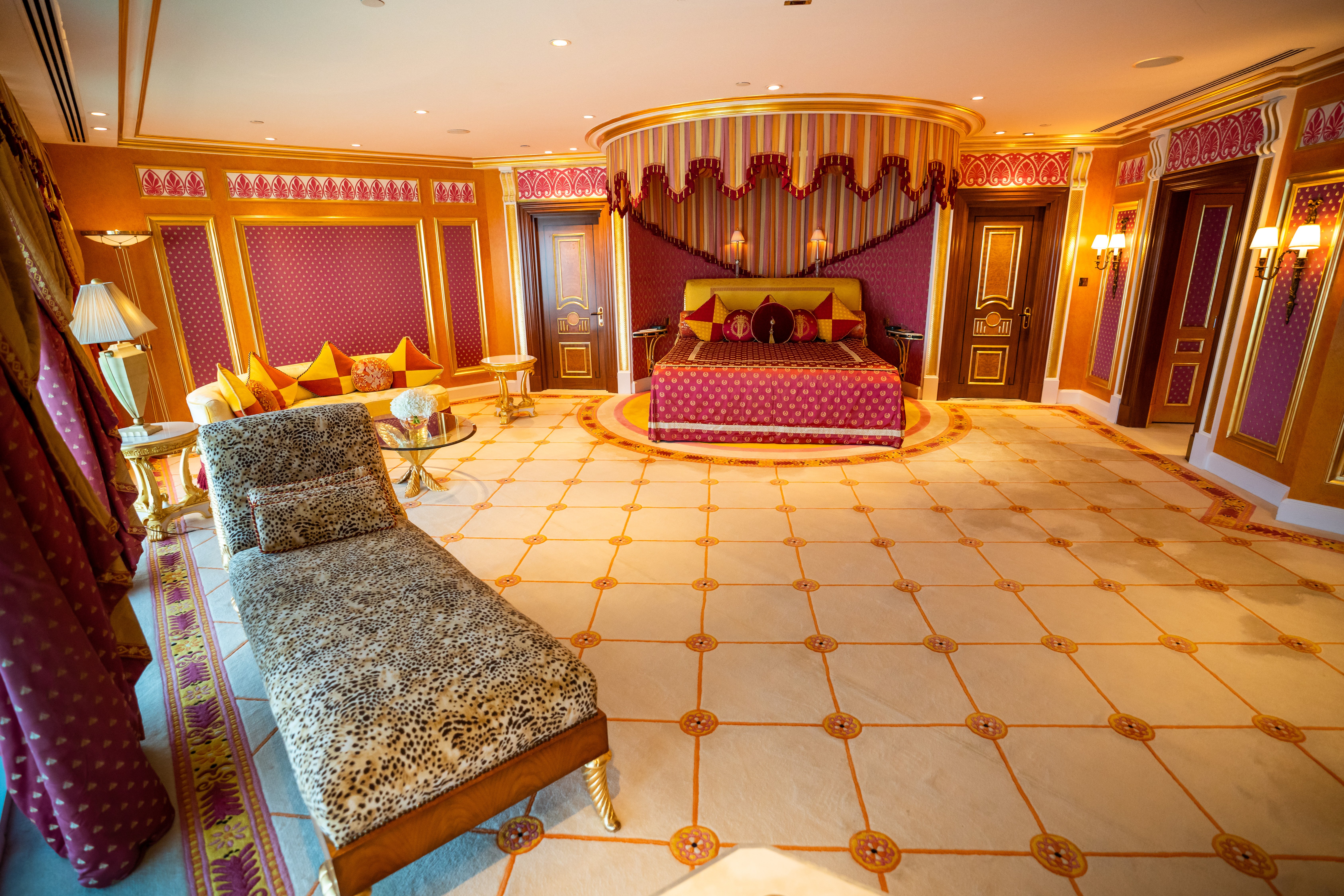 Luxurious bedroom with a chaise lounge, canopy bed, and gold accents.