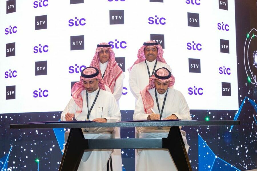 Men in Saudi attire signing documents near "stc" logos.