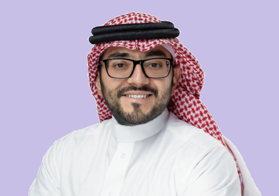 Man in keffiyeh smiling at camera with purple background.