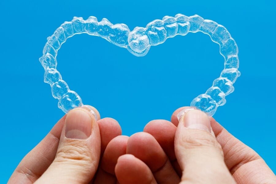 Clear aligner shaped like a heart held against a blue background.