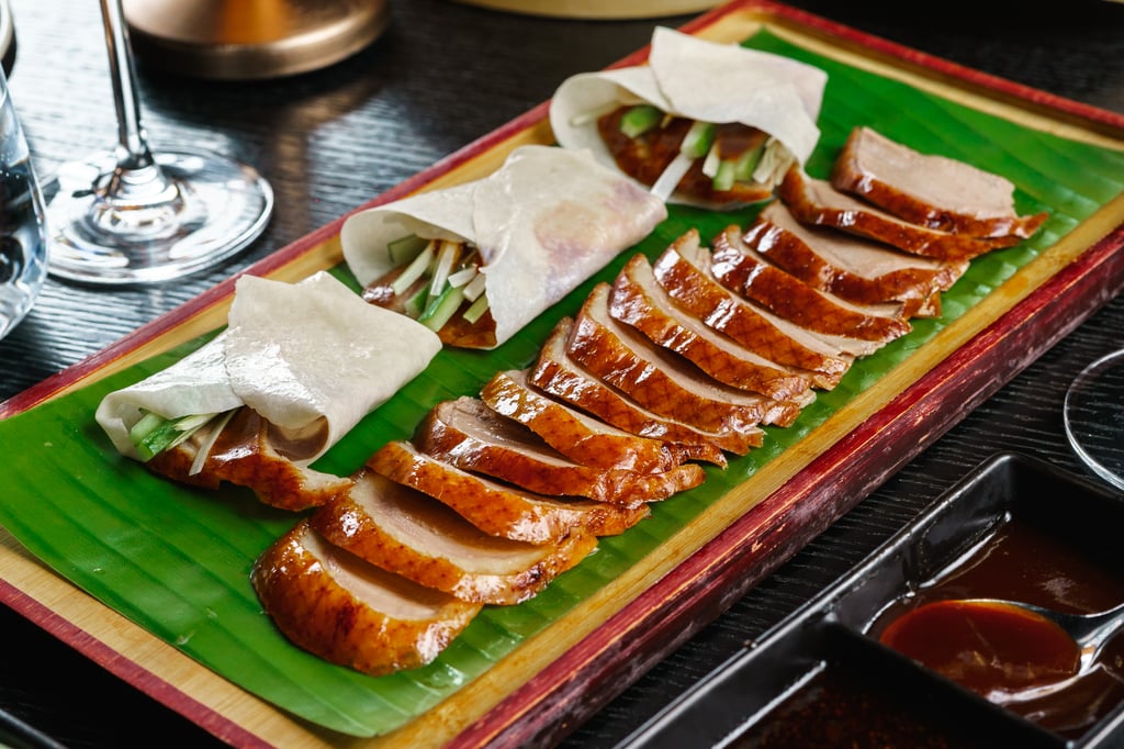 Sliced Peking duck with pancakes and scallions on a wooden platter.