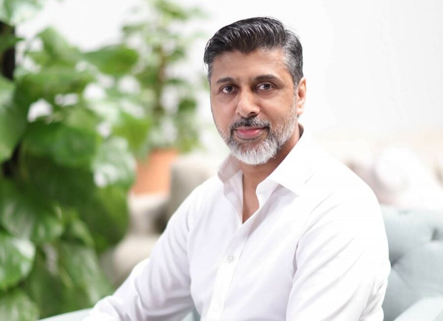 Graying man in white shirt looking at camera with plants in background.