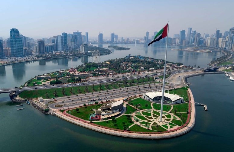 UAE flag on a tall flagpole, island with park, skyline in the background.