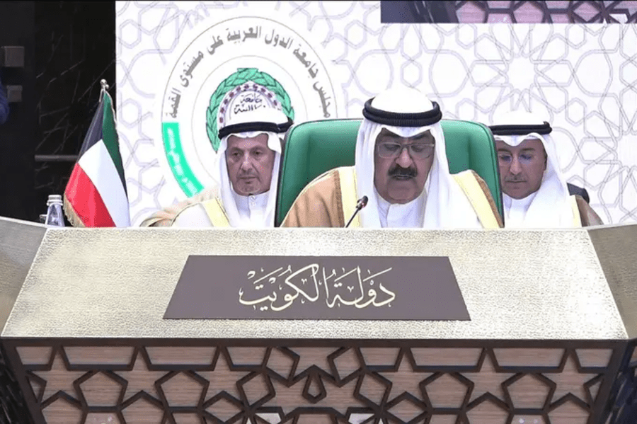 Three men in traditional Kuwaiti attire sitting at a table with a Kuwaiti flag.
