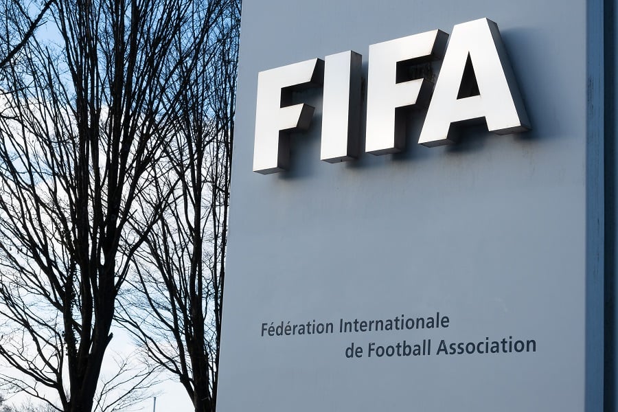 FIFA sign on gray wall with bare trees in background.