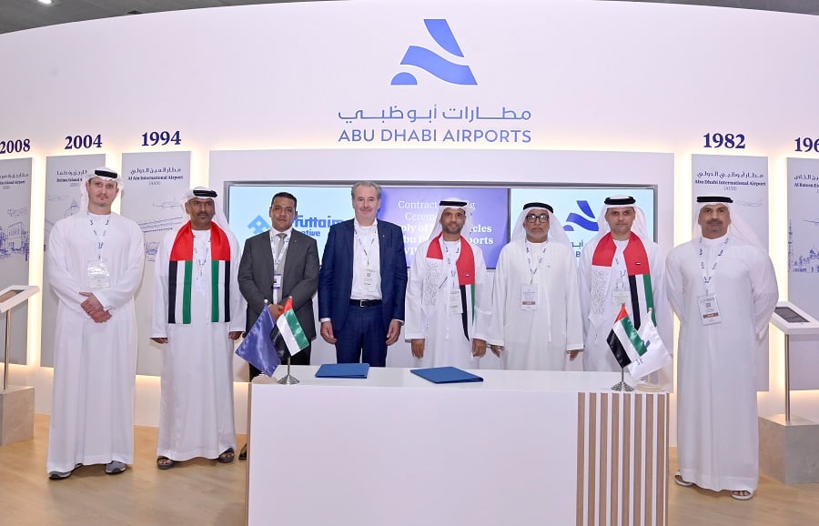 Men in thobes and suits at a signing ceremony with Abu Dhabi Airports branding.