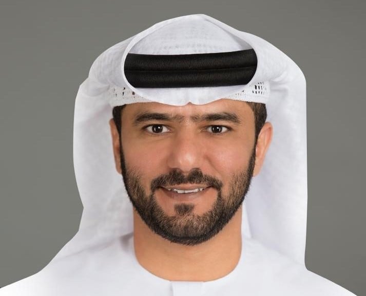 Smiling man in a white keffiyeh against a gray background.