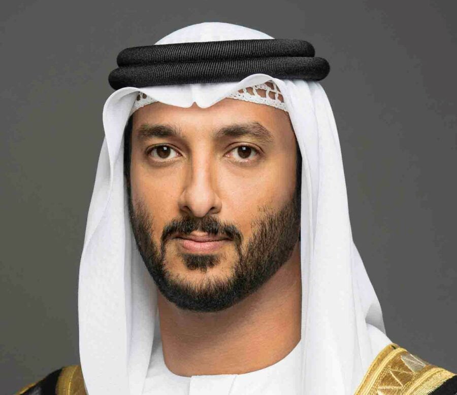 Man in white head covering with dark beard against a grey background.