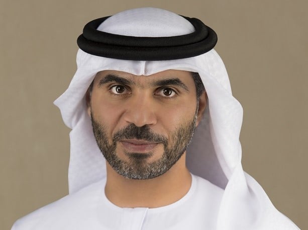 Man in a white kandura and black agal against a beige background.