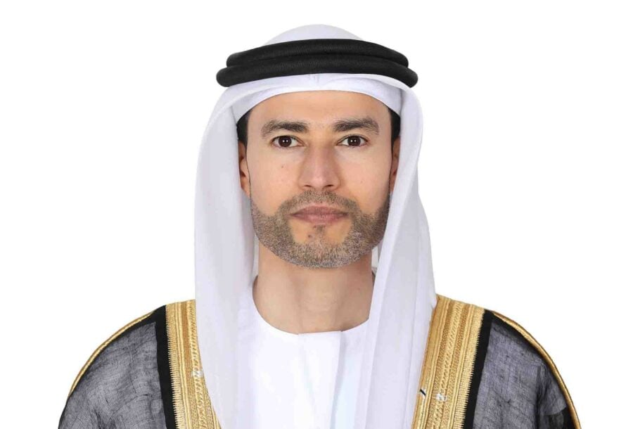 A man in a white headscarf and black robe poses against a white background.