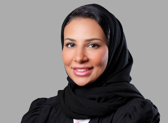 Woman in hijab smiling against grey background.