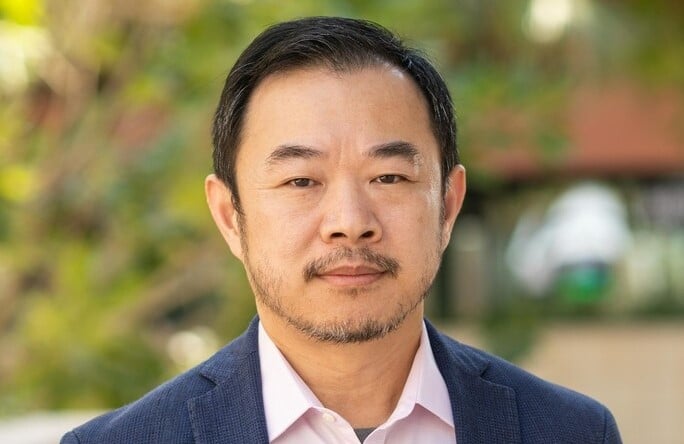 Man in a suit with a pink shirt, looking at the camera.