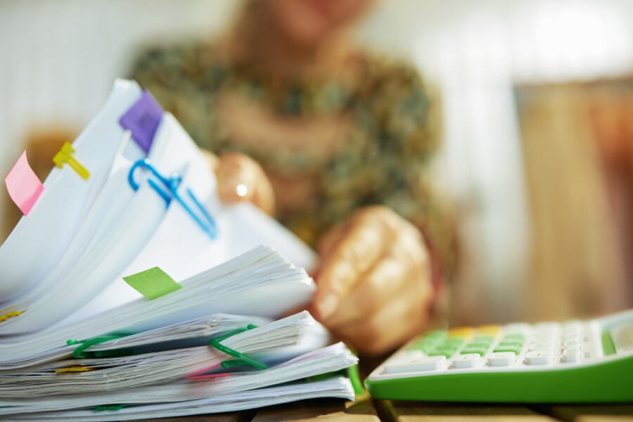 Person reviewing a stack of papers at a desk with a calculator.