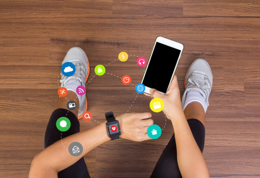 Person using a smartphone and smartwatch on a wooden floor.