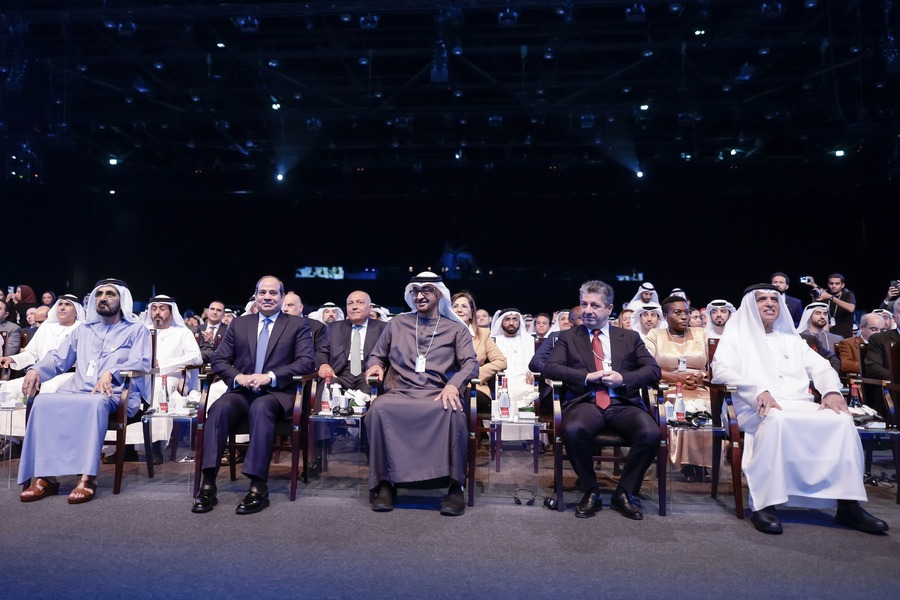 People in traditional attire attending an event in a dark auditorium.