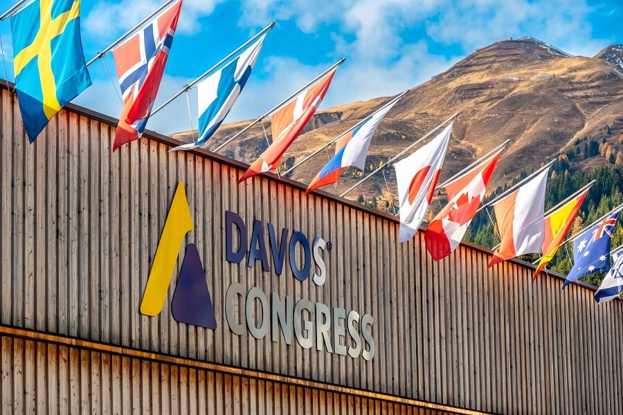 Davos Congress building with national flags and mountainous backdrop.