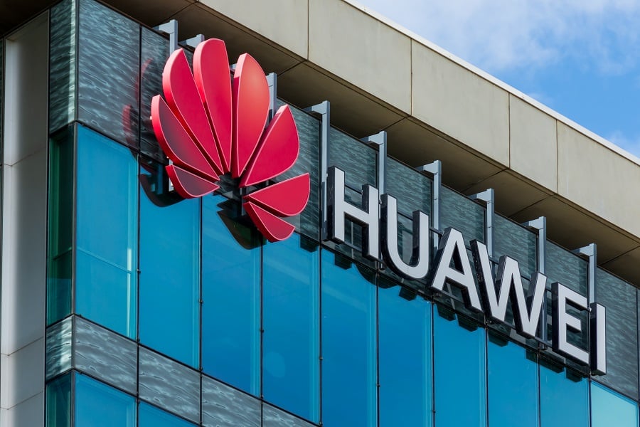 Huawei logo on a glass building against a bright sky.