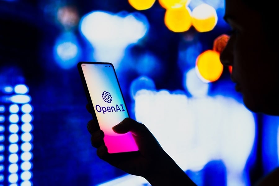 Smartphone displaying OpenAI logo held in hand with blurred background.