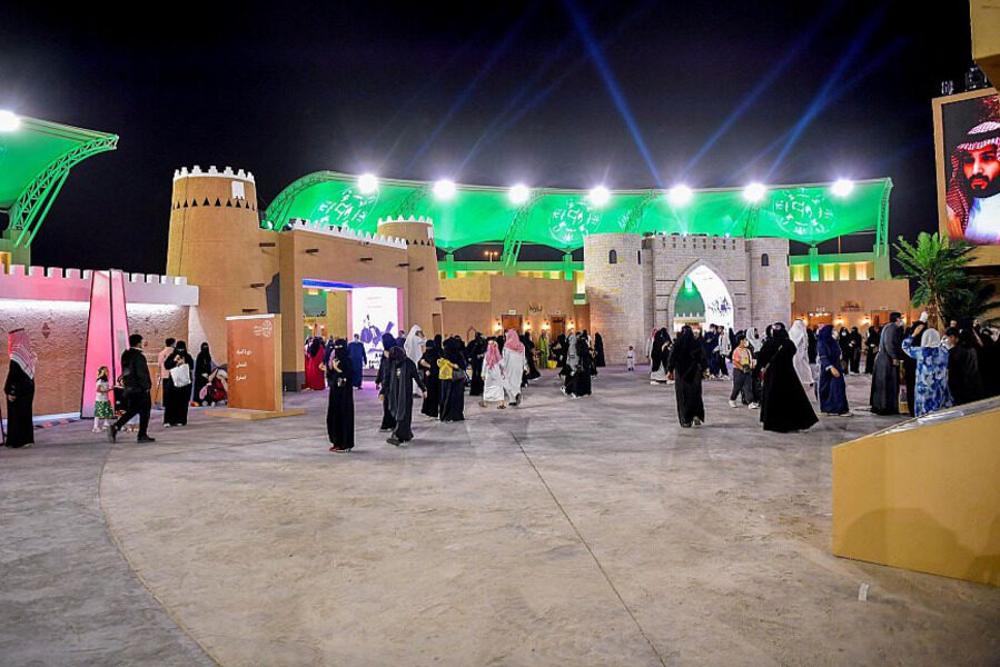 Nighttime event with traditional Middle Eastern buildings and stadium backdrop.