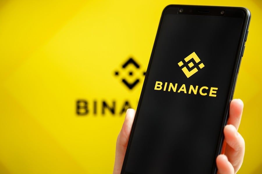 Smartphone displaying Binance logo against yellow backdrop.