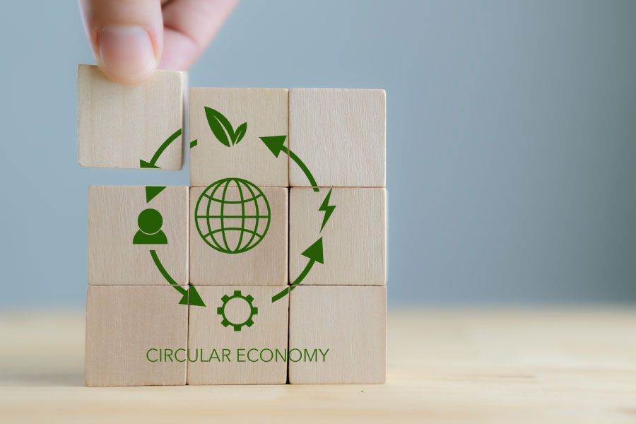 Hand placing a wooden cube onto a circular economy stack of icons.