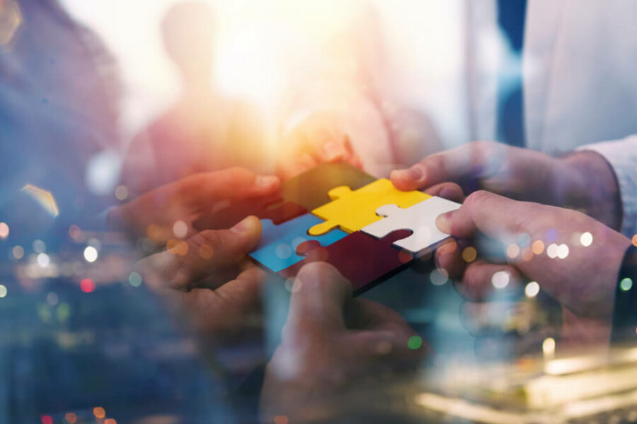 Four hands connecting puzzle pieces against a city background.