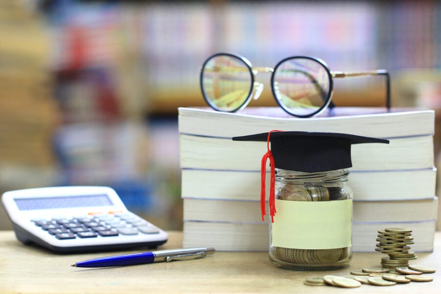 Glass jar of coins with a graduation cap on a desk.