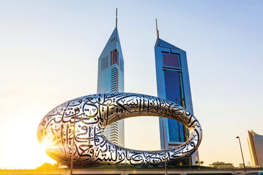 Metallic ring sculpture near skyscrapers at sunrise.