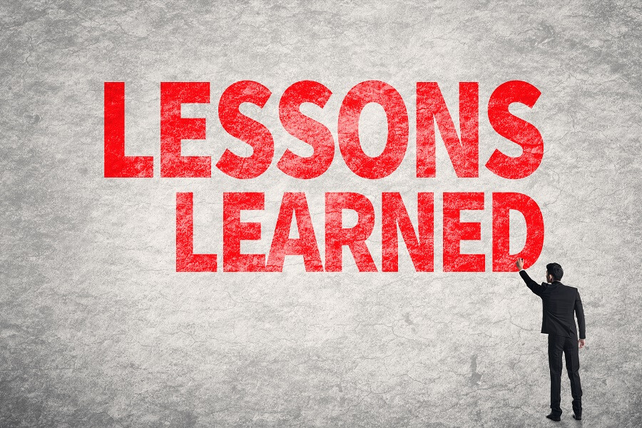 A man writes "LESSONS LEARNED" in red letters on a gray wall.