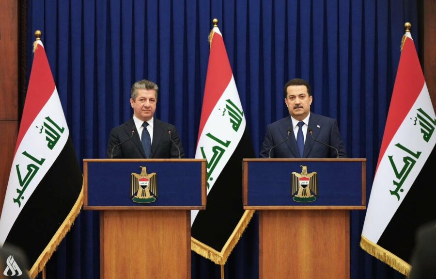 Two men in suits presenting with Iraqi flags in a formal setting.