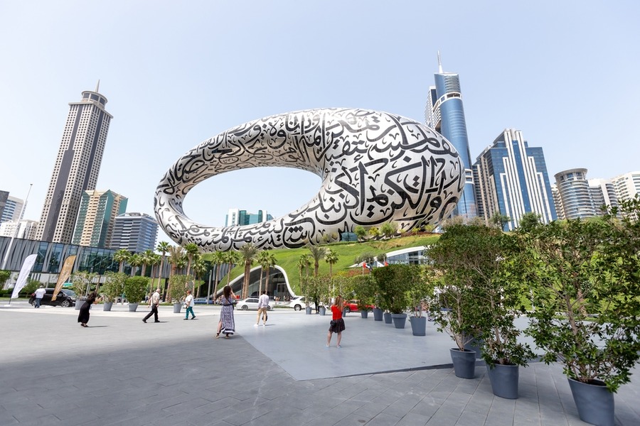 Large calligraphic sculpture in a plaza with modern skyscrapers nearby.