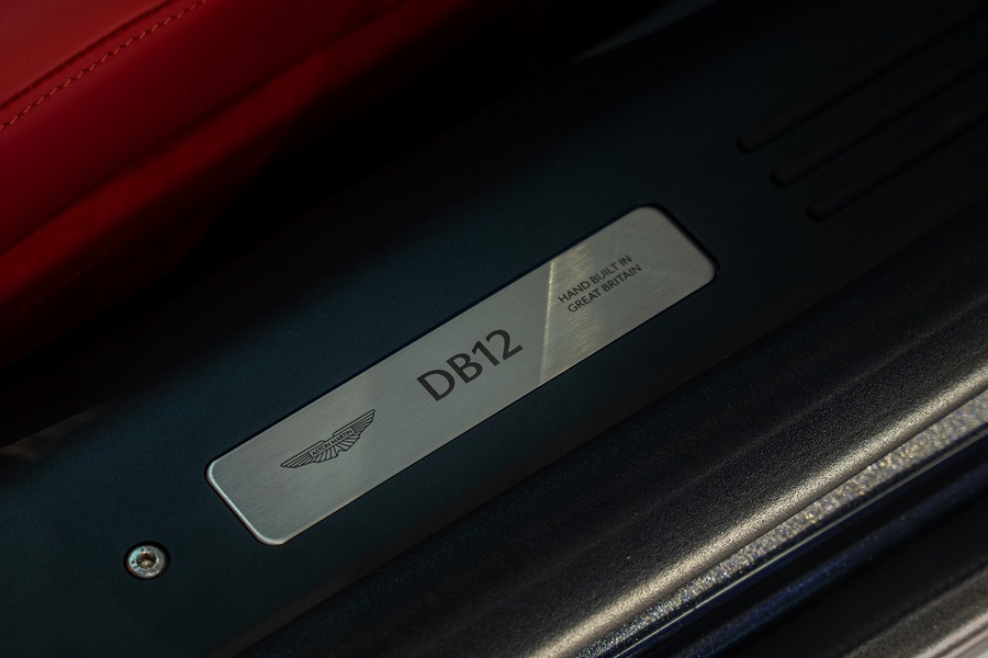 Metallic plate reads "DB12" in a luxury car interior.