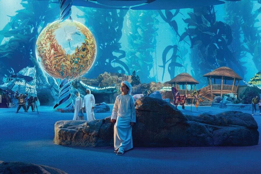 Boy looking at a sphere filled with kelp in an underwater setting.