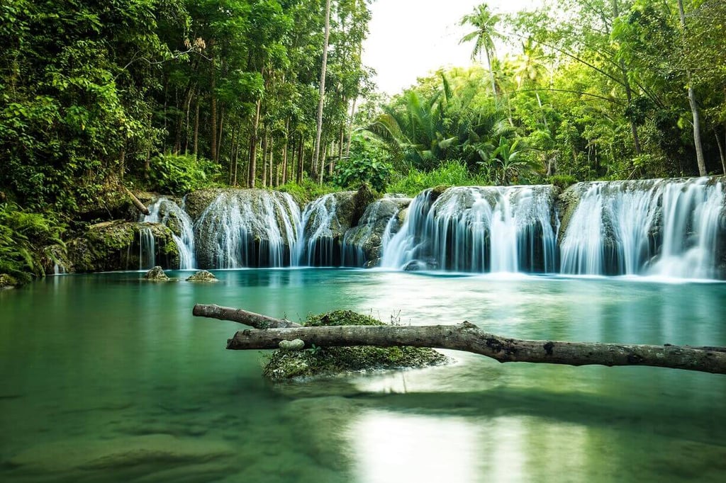 Waterfall cascading into a teal pool, surrounded by tropical vegetation.