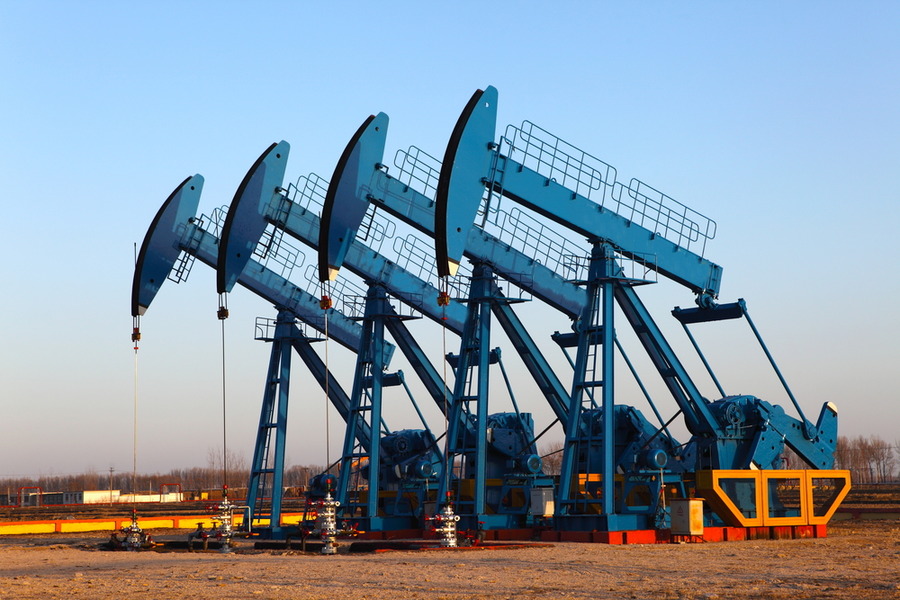 Oil derricks pumping in an open field under blue sky.