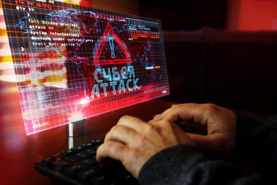 Hands typing on a keyboard, showing a cyberattack warning on a screen.