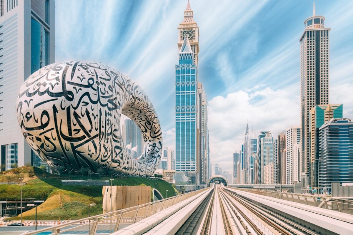Calligraphic structure next to train tracks in city with tall buildings.