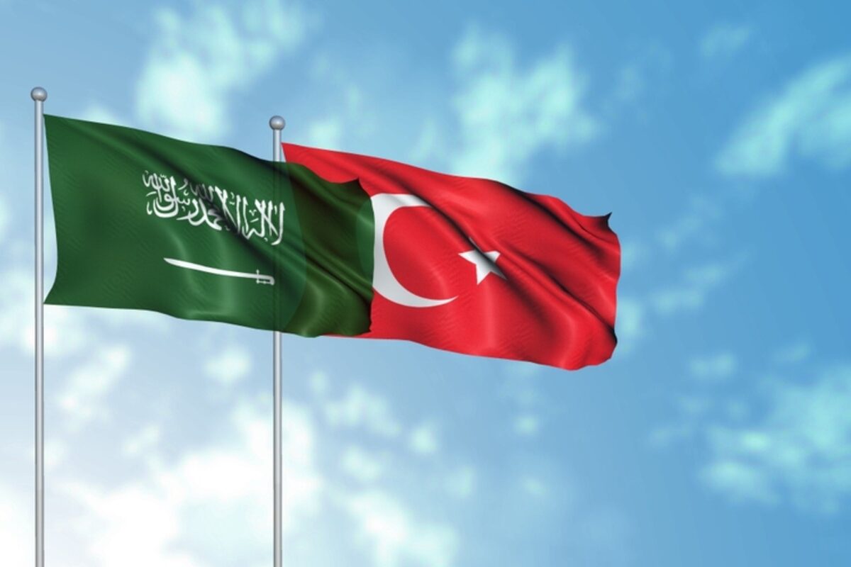 Flags of Saudi Arabia and Turkey wave in cloudy sky.