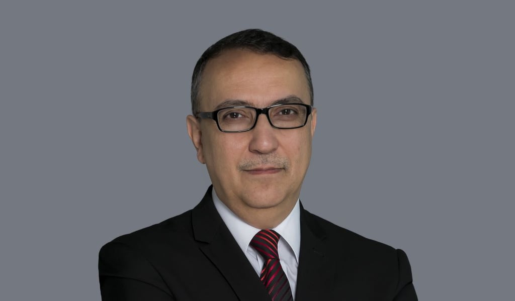 Man in glasses and suit with red tie on a gray background.