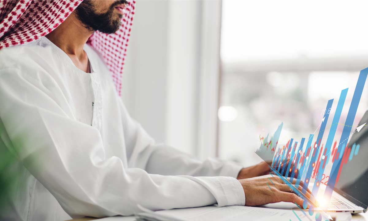 Arab man using a laptop with financial graphs on the screen.